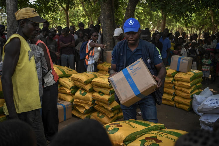 Aid workers deliver sacks of supplies to gathered crowd